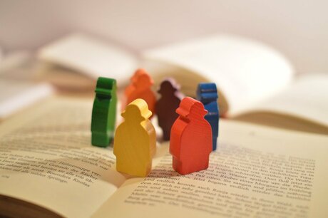 Six colourful meeple standing on the book "Ronia, the Robber's Daughter" by Michael Ende - Image source: Eigenmaterial